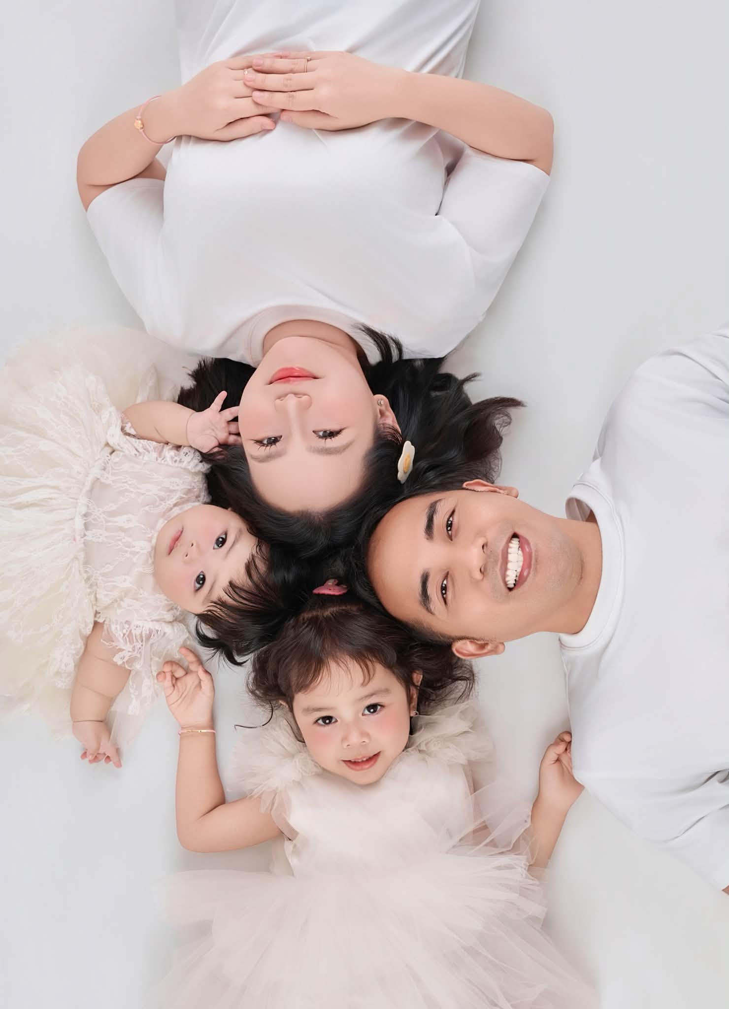 Ba mẹ và hai bé nằm cạnh nhau trong bộ ảnh gia đình sáng màu